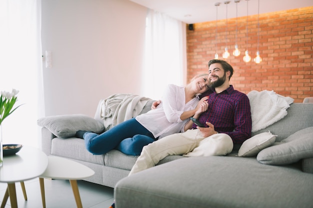 Couple souriant, regarder la télévision à la maison