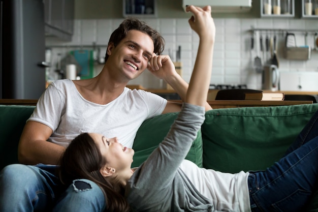 Couple souriant s&#39;amuser avec smartphone prenant selfie à la maison