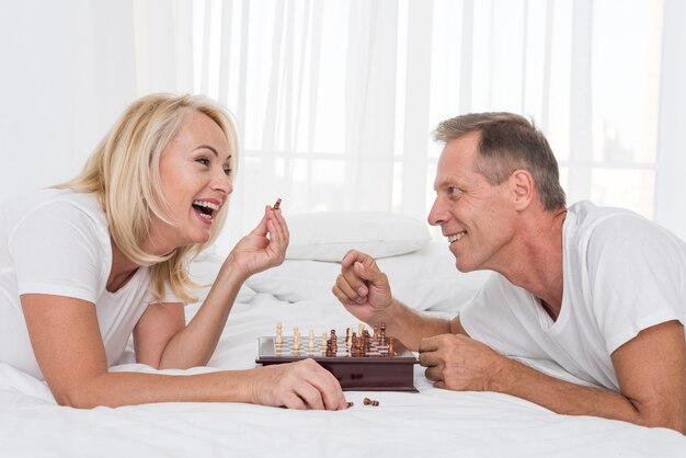 Couple souriant smileys jouant aux échecs dans la chambre