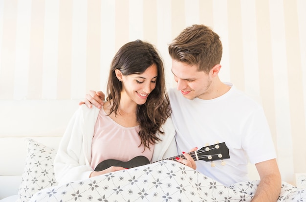 Photo gratuite couple souriant avec ukulele sur le lit