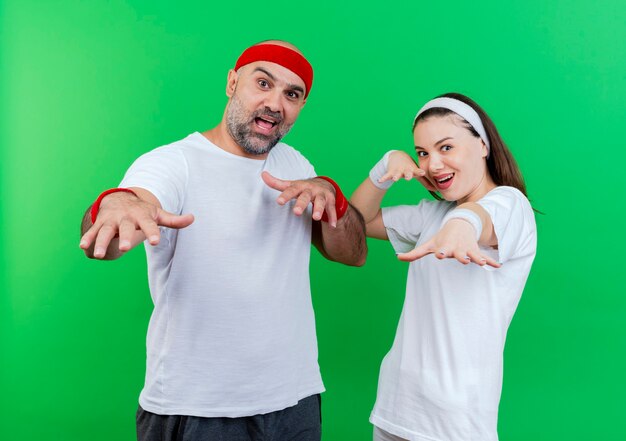 Couple sportif adulte impressionné portant un bandeau et des bracelets à la fois étendant les mains vers