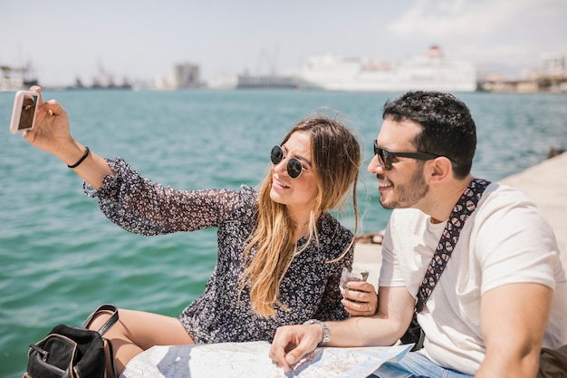 Couple, touriste, séance, carte, jetée, prendre, selfie, sur, téléphone portable