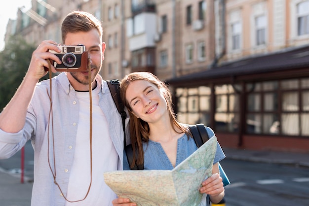 Couple de touristes posant à l'extérieur avec caméra et carte