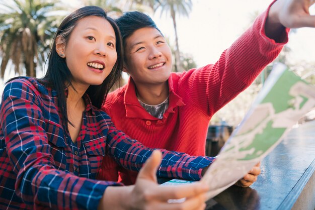 Couple de voyageurs asiatiques tenant une carte et à la recherche d'itinéraires.