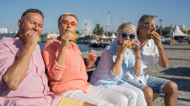 Photo gratuite couples aînés appréciant des hamburgers ensemble à la plage