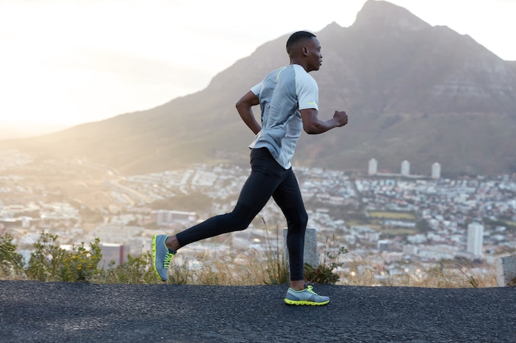 Photo gratuit le coureur sportif à la peau foncée et autodéterminé porte des vêtements de sport, court sur de longues distances sur une route de montagne, apprécie l'air frais, se sent énergique et motivé. concept de personnes, de style de vie et de sport