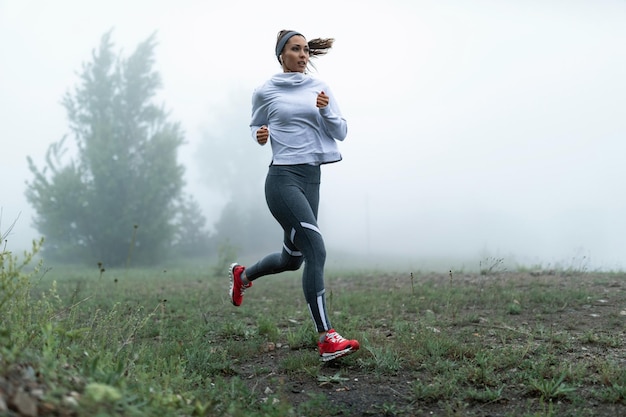 Coureuse déterminée faisant du jogging dans la brume déposée le matin Espace de copie