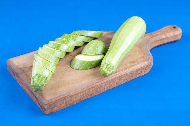 Courgettes vertes fraîches et tranches placées sur planche de bois.