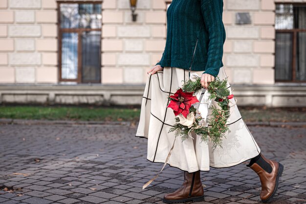 Couronne de Noël entre les mains d'une femme élégante à pied