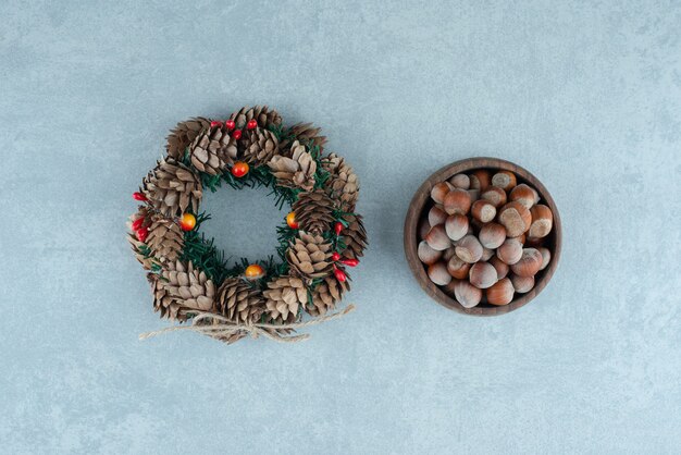 Couronne de pomme de pin et bol de noisettes sur marbre.