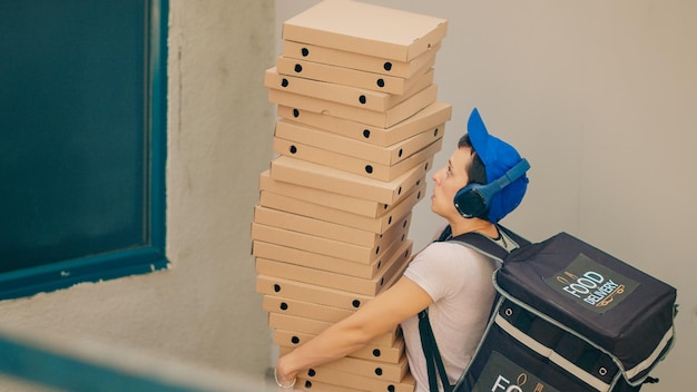 Photo gratuite courrier alimentaire maladroit essayant d'attraper des boîtes de pizza qui tombent, agissant effrayé et fuyant la porte d'entrée du client après avoir laissé tomber le repas de livraison de restauration rapide. transporteur peur avec un mauvais service. prise de vue à main levée.