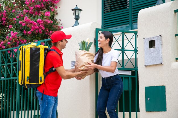 Courrier amical avec sac à dos isotherme donnant un colis de l'épicerie au client. Concept de service d'expédition ou de livraison