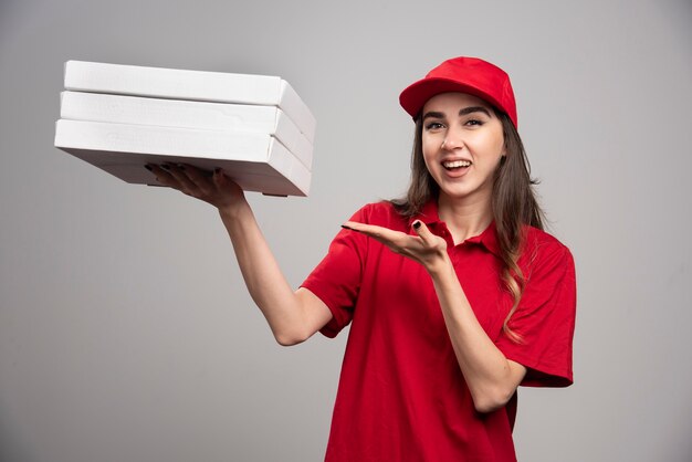 Courrier femelle tenant des boîtes à pizza sur un mur gris.