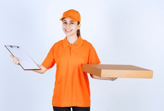 Courrier femelle en uniforme orange tenant une boîte de pizza à emporter et un carnet d'adresses.