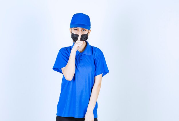 Courrier féminin en masque et uniforme bleu fermant la bouche et demandant le silence.