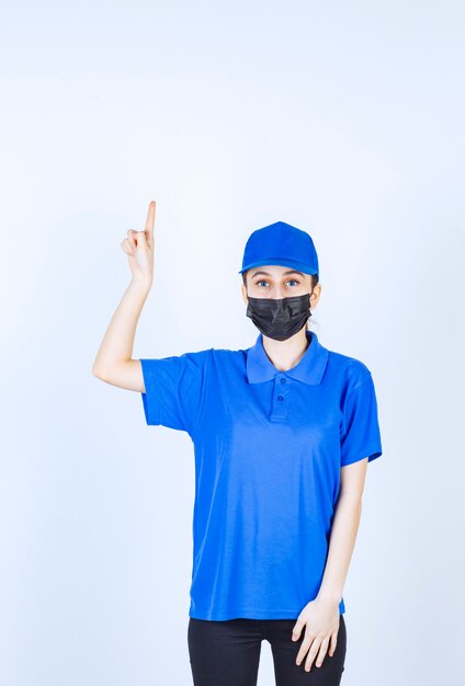 Courrier féminin en masque et uniforme bleu montrant quelque chose ci-dessous