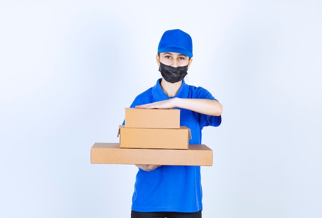 Courrier féminin en masque et uniforme bleu tenant un stock de boîtes en carton.