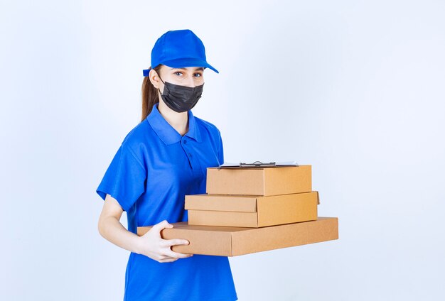Courrier féminin en masque et uniforme bleu tenant un stock de boîtes en carton