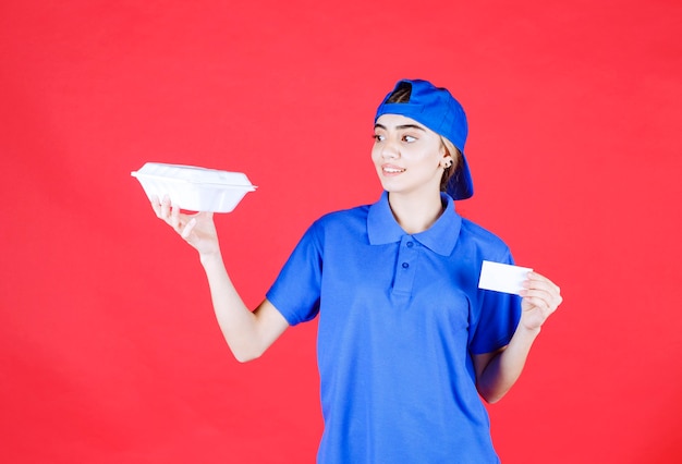 Courrier féminin en uniforme bleu tenant une boîte à emporter blanche et présentant sa carte de visite.