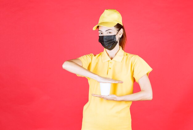 Courrier féminin en uniforme jaune et masque noir tenant une tasse à emporter