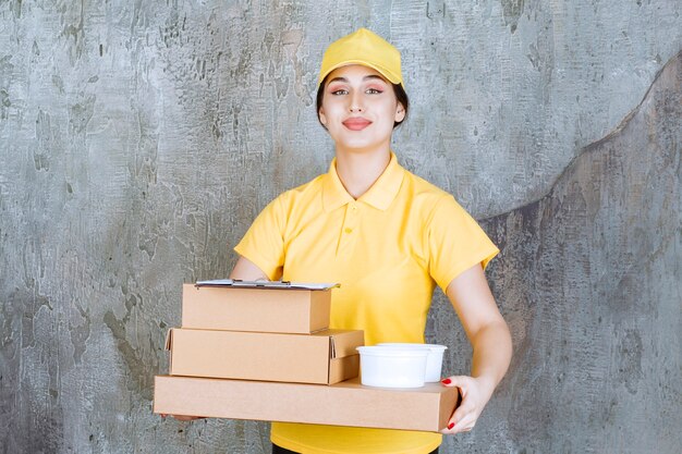 Courrier féminin en uniforme jaune offrant plusieurs boîtes en carton et gobelets à emporter.