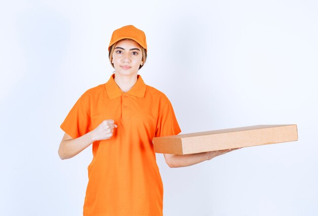 Courrier féminin en uniforme orange livrant une boîte en carton et montrant le signe de la main de satisfaction