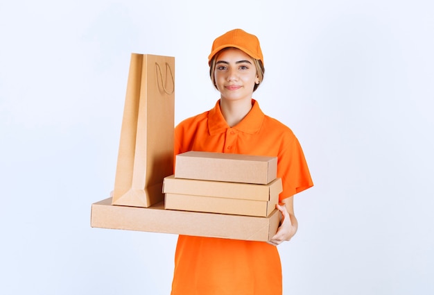 Courrier féminin en uniforme orange tenant un stock de colis en carton et de sacs à provisions