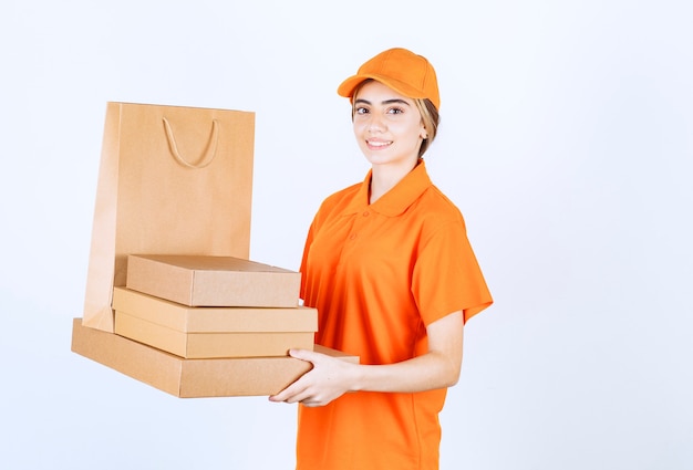 Courrier féminin en uniforme orange tenant un stock de colis en carton et de sacs à provisions