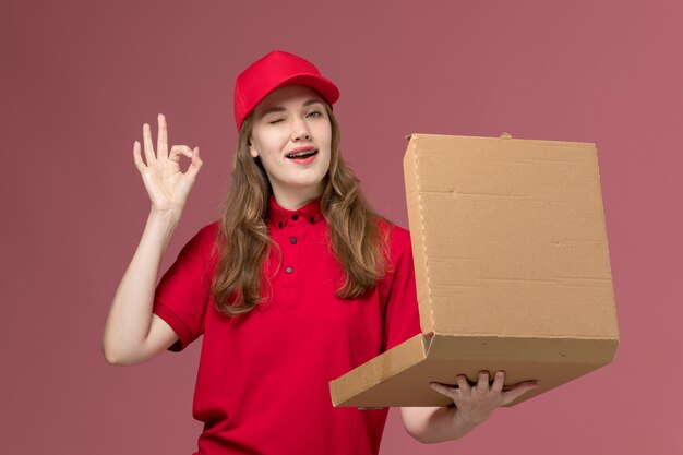 Courrier féminin en uniforme rouge tenant et ouvrant la boîte de nourriture sur rose, service uniforme livrant des travailleurs