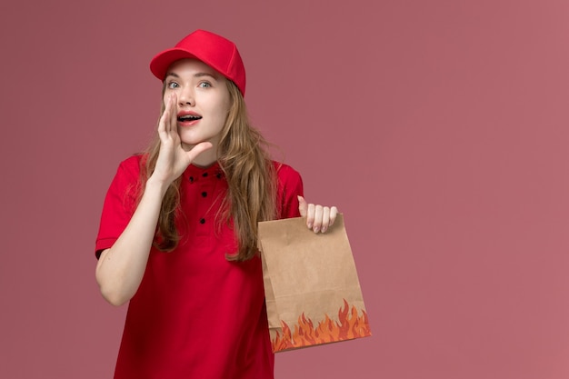 Courrier féminin en uniforme rouge tenant le paquet de nourriture et chuchotant sur la livraison de travailleur de service uniforme rose clair, travail