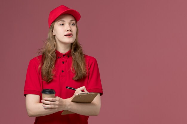 Courrier féminin en uniforme rouge tenant une tasse de café et un bloc-notes sur rose, travailleur de travail de livraison de service uniforme