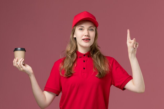 Courrier féminin en uniforme rouge tenant une tasse de café marron avec un doigt sur rose clair, travail uniforme de la prestation des travailleurs des services