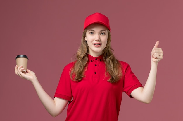 Courrier féminin en uniforme rouge tenant une tasse de café sur rose clair, prestation de services de travailleur uniforme de travail