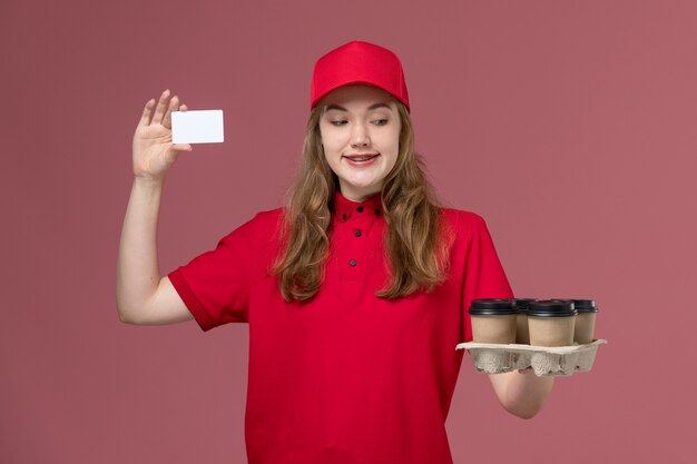 Courrier féminin en uniforme rouge tenant des tasses de café de livraison marron et carte sur rose, un service uniforme livrant des travailleurs