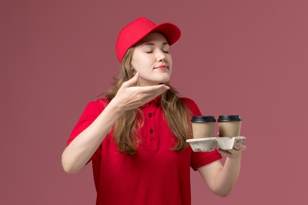 Courrier féminin en uniforme rouge tenant des tasses à café les sentant sur rose, service uniforme livrant des travailleurs