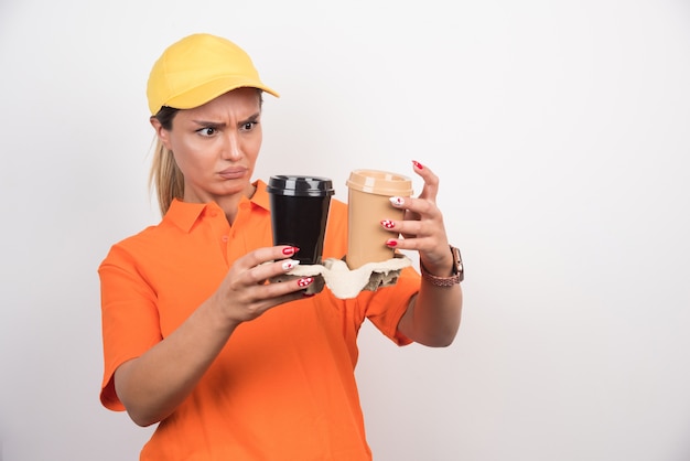 Photo gratuite courrier femme blonde regardant deux tasses de cafés sur un mur blanc.