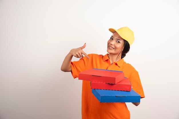 Courrier de femme pointant sur des pizzas sur un mur blanc.