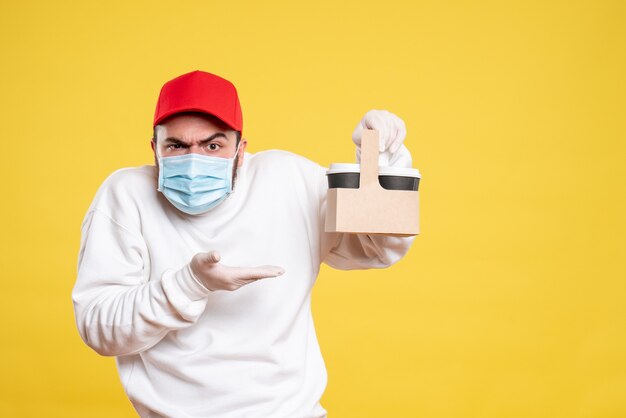 courrier mâle en masque tenant un café de livraison sur jaune