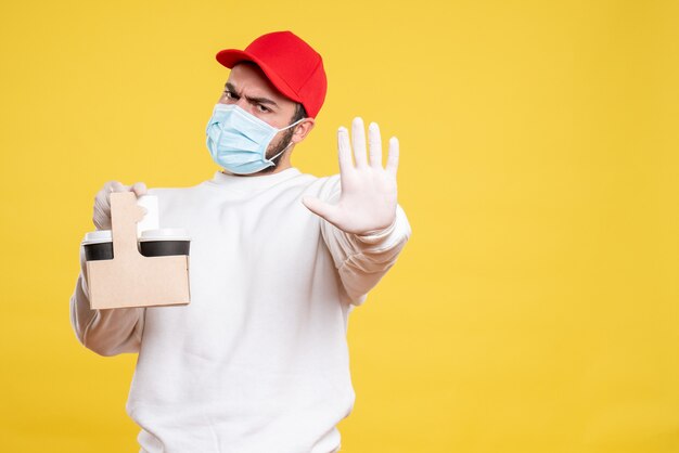 courrier mâle en masque tenant un café de livraison sur jaune