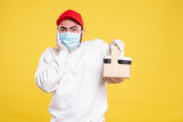 courrier mâle en masque tenant un café de livraison sur jaune