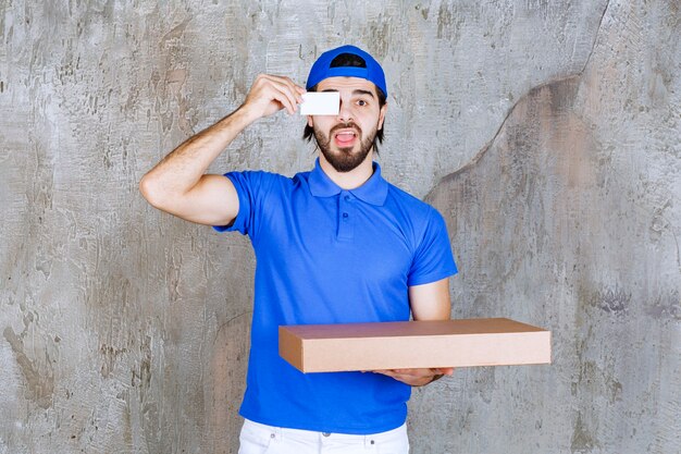 Courrier masculin en uniforme bleu portant une boîte en carton et présentant sa carte de visite.