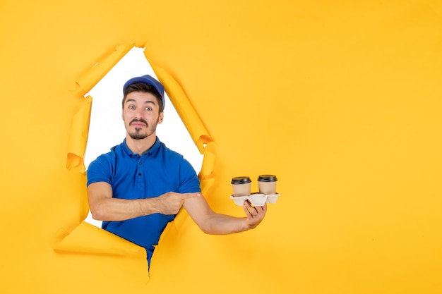 Courrier masculin vue de face en uniforme bleu tenant des tasses à café sur un espace jaune