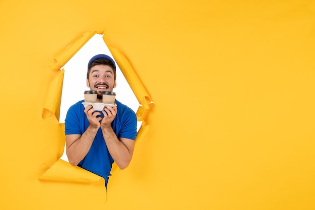 Courrier masculin vue de face en uniforme bleu tenant des tasses à café sur un espace jaune