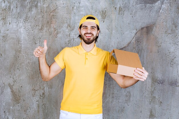 Courrier en uniforme jaune tenant une boîte en carton ouverte et appréciant le produit.