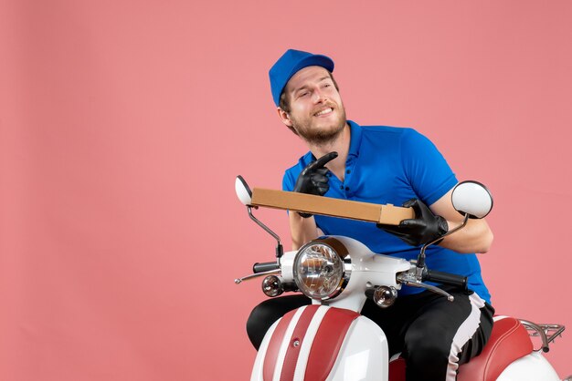 Coursier mâle vue de face assis sur un vélo et tenant une boîte de nourriture sur rose