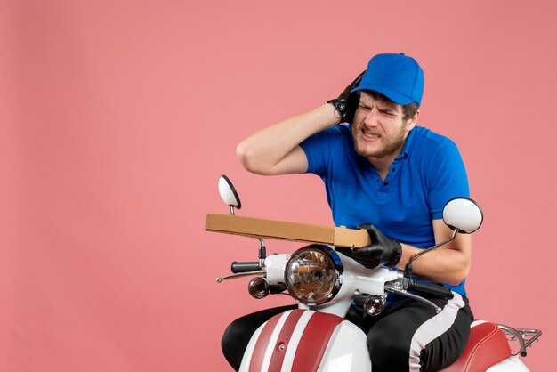 Coursier mâle vue de face assis sur un vélo et tenant une boîte à pizza sur le rose