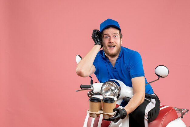 Coursier mâle vue de face assis sur un vélo et tenant des tasses à café sur le rose