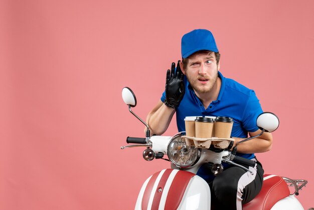 Coursier mâle vue de face assis sur un vélo et tenant des tasses à café sur le rose