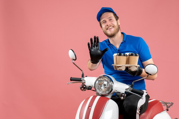 Coursier mâle vue de face assis sur un vélo et tenant des tasses à café sur le rose