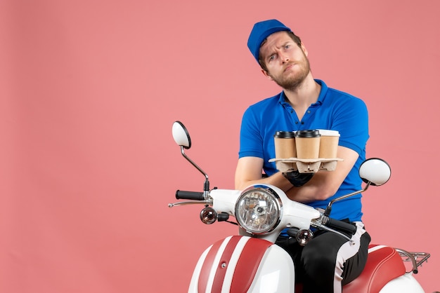 Coursier mâle vue de face assis sur un vélo et tenant des tasses à café sur le rose